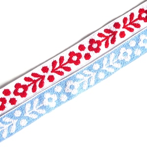 May include: Two white cotton ribbons with embroidered floral designs. One ribbon has red flowers and the other has blue flowers.