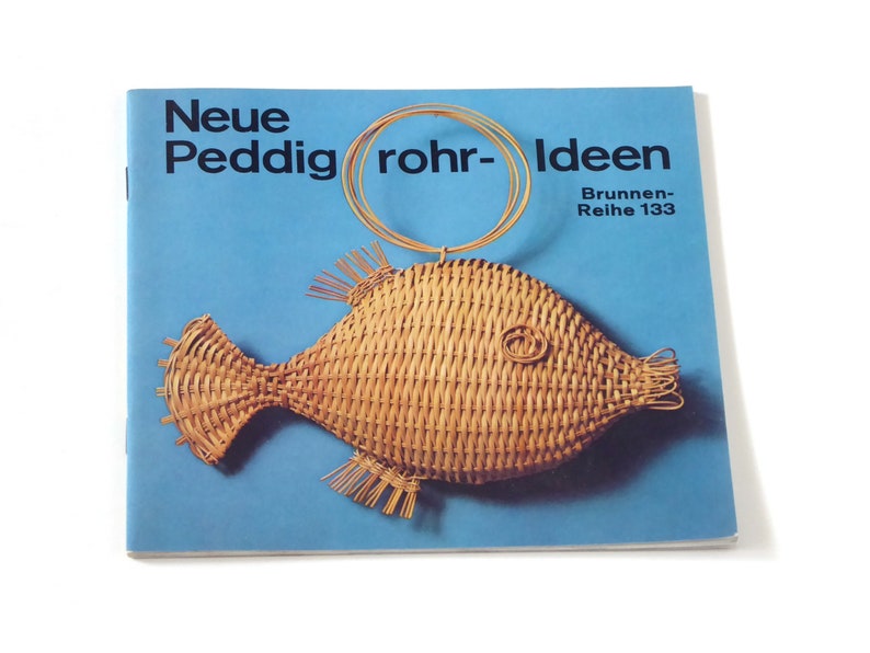 Puede incluir: Un folleto azul con el t&iacute;tulo "Neue Peddigrohr-Ideen" y el texto "Brunnen-Reihe 133". La portada presenta un pez de mimbre tejido con un anillo de alambre.