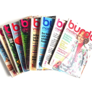 May include: A stack of vintage German fashion magazines titled "Burda Moden" with colorful covers featuring various fashion styles and models.