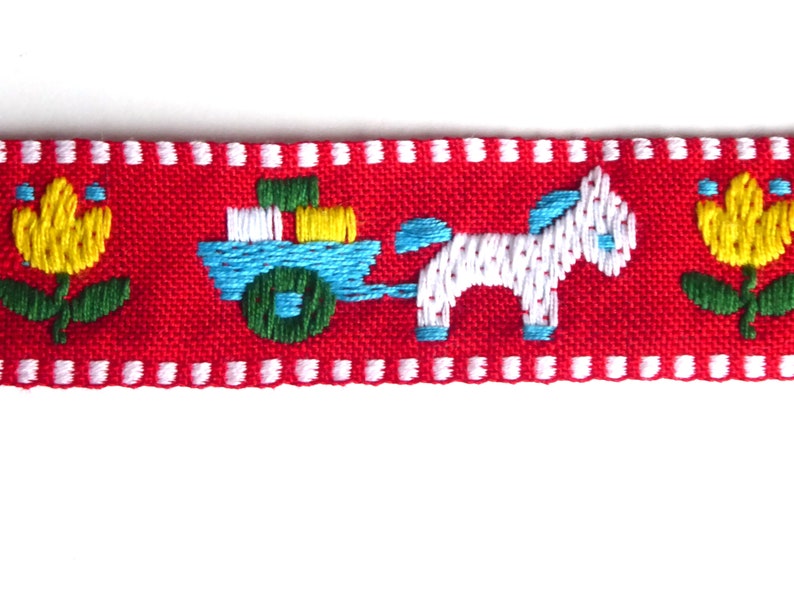 May include: Red fabric ribbon with a white horse pulling a blue wagon with yellow and green blocks, and yellow flowers with green stems on either side.