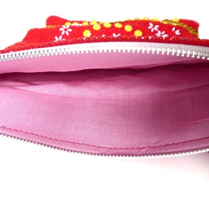 K&ouml;nnte beinhalten: Rote Rei&szlig;verschlusstasche mit rosa Stofffutter. Die Tasche ist mit wei&szlig;en Blumen und gelben Punkten verziert.