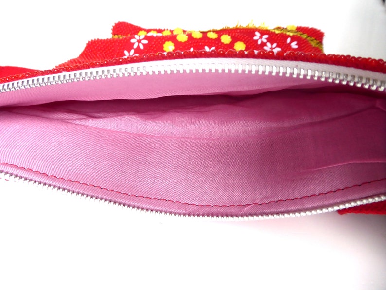 K&ouml;nnte beinhalten: Rote Rei&szlig;verschlusstasche mit rosa Stofffutter. Die Tasche ist mit wei&szlig;en Blumen und gelben Punkten verziert.