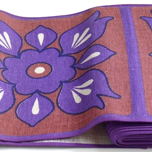 May include: A purple and brown floral patterned floor mat rolled up. The mat has a purple border and is made of a woven material.