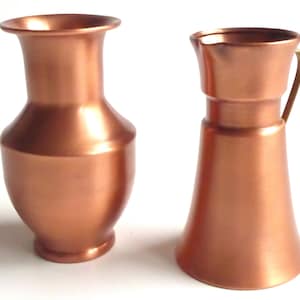 Könnte beinhalten: Zwei Kupfervasen, eine mit einem ausgestellten oberen Rand und einem Henkel, die andere mit einem schmalen Hals und einem abgerundeten Boden.