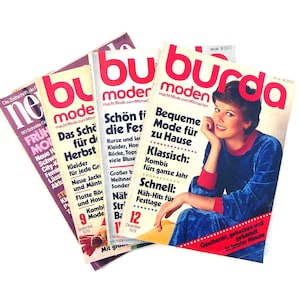 Puede incluir: Cuatro ejemplares de la revista de moda alemana Burda Moden. Las revistas están apiladas una encima de la otra. La revista de arriba tiene una foto de una mujer con un suéter azul y un cuello rojo. El texto de la portada dice "Burda Moden macht Mode zum Mitmachen" y "Moda cómoda para el hogar".