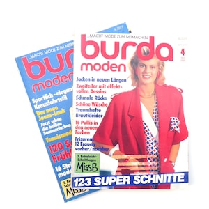 Può includere: Due copie della rivista Burda Moden, una rivista di moda tedesca. La copertina della rivista a destra presenta una donna che indossa una giacca rossa con una camicia a righe bianche e rosse. Il testo sulla copertina recita "Burda Moden" e "123 Super Schnitte".