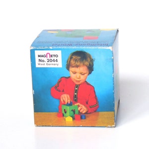 May include: A box for a wooden toy called "Intelligenz-Würfel" by Magneto No. 2044, West Germany. The box shows a child playing with the toy, which is a colorful cube with different shapes and colors.