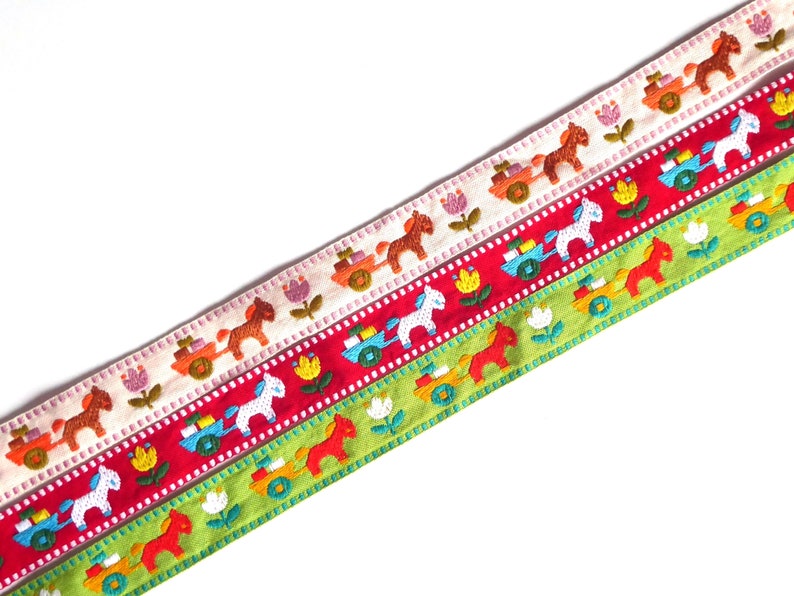 May include: Three colorful ribbon trims with embroidered designs of horses pulling carts. The ribbons are white with orange and brown horses, red with pink and blue horses, and green with orange and red horses.