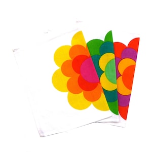 Könnte beinhalten: Drei weiße Geschirrtücher mit einem farbenfrohen Blumendesign. Die Blume besteht aus überlappenden Kreisen in den Farben Gelb, Orange, Rot, Rosa, Grün und Lila.