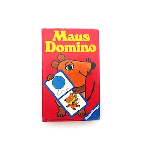 以下が含まれることがあります： ラベンスバーガーの「Maus Domino」の赤い箱。箱には、青い風船とネズミのイラストが描かれたドミノタイルを持つ漫画のネズミが描かれています。「Maus Domino」の文字は黄色です。