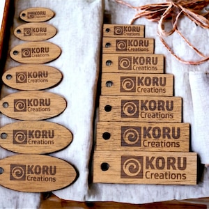 May include: A set of wooden tags with the text "KORU Creations" and a stylized swirl design. The tags are different sizes and shapes, with some being oval and others rectangular.