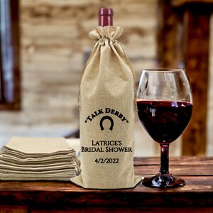 May include: A burlap wine bag with a horseshoe design and the text "Talk Derby" and "Latrice's Bridal Shower 4/2/2022".