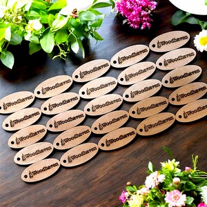 May include: A collection of 20 oval-shaped wooden tags with the text "Woodhaven" and a small pine tree design engraved on each tag.