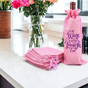 May include: Pink burlap wine bottle bags with a purple design that says "Wine a little laugh a lot".