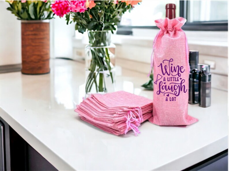 May include: Pink burlap wine bottle bags with a purple design that says "Wine a little laugh a lot".