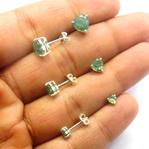 May include: A set of four silver earrings with green gemstone accents. The earrings feature a variety of shapes, including round and heart-shaped stones.