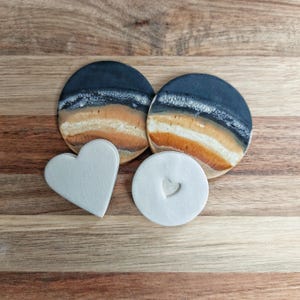 Könnte beinhalten: Zwei runde Untersetzer in Schwarz und Braun mit einem weißen Herzdesign. Zwei weiße herzförmige Untersetzer mit einem kleinen Herz-Ausschnitt.