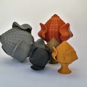 Puede incluir: Cinco remates decorativos impresos en 3D en varios colores y diseños. Los remates están hechos de un material plástico texturizado y tienen una variedad de formas, incluyendo una flor, un cono y una esfera.