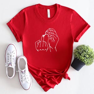 May include: Red short-sleeved t-shirt with a white line drawing of two hands making a rude gesture.