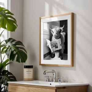 Op de afbeelding: Zwart-witfoto van een Schotse hooglander die op een toilet zit en een krant leest. De krantenkoppen luiden "PROTEST IS AT", de foto is ingelijst in een licht houten lijst.