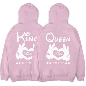 May include: Two pink hoodies with white text and graphics. One hoodie says "King" with a heart and "Since 12.12.20" and the other says "Queen" with a heart and "Since 12.12.2012".