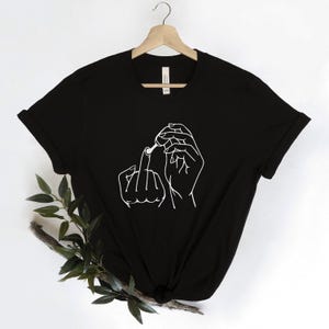 May include: Black t-shirt with a white line drawing of a hand holding a cigarette and giving the middle finger.
