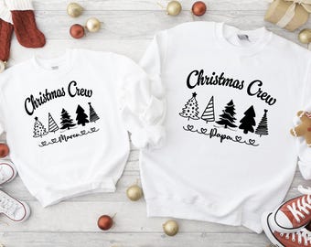 Puede incluir: Dos sudaderas blancas de la tripulación de Navidad con diseños de árboles de Navidad negros y las palabras "Christmas Crew" y "Papa" y "Momma" en ellas.