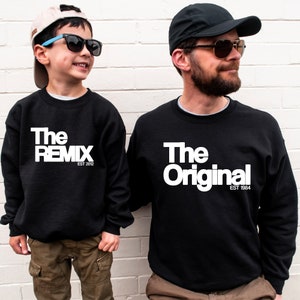 Könnte beinhalten: Zwei schwarze Sweatshirts mit weißem Text. Ein Sweatshirt sagt "The Remix Est 2012" und das andere sagt "The Original Est 1984".