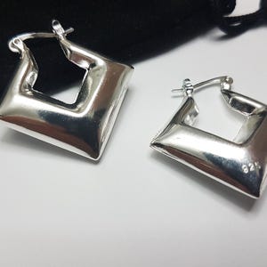 May include: A pair of polished silver hoop earrings with a distinct square or diamond-shaped silhouette. The earrings feature a hinged post closure mechanism and are stamped with the 925 hallmark, indicating sterling silver composition.