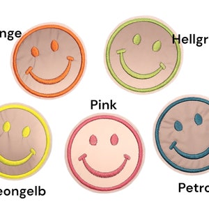 Könnte beinhalten: Eine Sammlung von gestickten Smiley-Gesicht-Patches in verschiedenen Farben. Die Patches umfassen Orange, Hellgrün, Gelb, Pink und Blau. Jeder Patch hat einen beigen Hintergrund und ein lächelndes Gesicht.