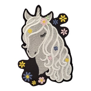 Könnte beinhalten: Weiß gestickter Einhornkopf mit einer rosa Blütenkrone und bunten Blumen drumherum. Das Einhorn befindet sich auf einem schwarzen Hintergrund.