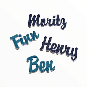 Könnte beinhalten: Vier gestickte Bügelbilder mit den Namen Moritz, Finn, Henry und Ben in Blau und Weiß.