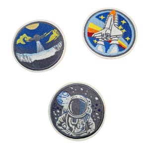 Könnte beinhalten: Drei gestickte Bügelbilder mit Weltraummotiven. Ein Patch zeigt ein blaues und weißes Raumschiff mit orangefarbenen Flammen. Ein weiterer Patch zeigt einen blauen und weißen Astronauten in einem Raumanzug. Der dritte Patch zeigt ein blaues und weißes UFO, das über einen Planeten fliegt.