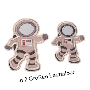 Könnte beinhalten: Zwei gestickte Bügelbilder von Astronauten in verschiedenen Größen. Der Text "In 2 Größen bestellbar" befindet sich unter den Patches.