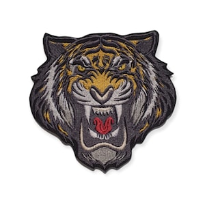 Könnte beinhalten: Gestickter Aufnäher mit einem brüllenden Tigerkopf. Der Aufnäher hat ein Farbschema aus Schwarz, Grau und Gold, mit einer roten Zunge im geöffneten Maul. Die Augen des Tigers sind gelb, und das Design ist detailliert.