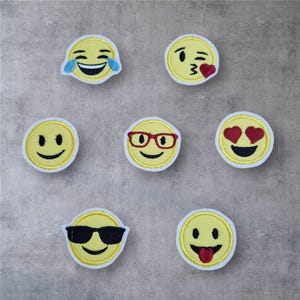 Könnte beinhalten: Eine Sammlung gelber Emoji-Patches mit verschiedenen Ausdrücken, darunter Lachen mit Tränen, Zwinkern mit Herz, Lächeln, Tragen einer Brille, Herzen für die Augen, Tragen einer Sonnenbrille und Herausstrecken der Zunge. Jeder Patch hat einen weißen Rand.