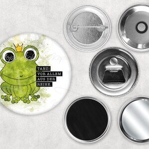 Könnte beinhalten: Ein weißer Knopf mit einem grünen Frosch, der eine goldene Krone trägt. Der Frosch sitzt auf einem Aquarellhintergrund mit dem Text "TANZ! VOR ALLEM AUS DER REihe."