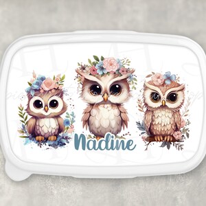 Könnte beinhalten: Weiße Lunchbox mit einem floralen Design mit drei Eulen mit Blumenkränzen. Der Name "Nadine" ist in Blau unter den Eulen geschrieben.