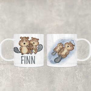 Könnte beinhalten: Weiße Keramiktasse mit einem braunen Biber-Familienmotiv und dem Namen "FINN" auf der Vorderseite. Die Rückseite der Tasse zeigt einen Biber, der in einem blauen Teich schwimmt.