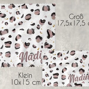 Könnte beinhalten: Zwei weiße Stoffquadrate mit einem rosa-schwarzen Leopardenmuster und goldenem Glitzer. Das größere Quadrat ist 17,5 cm x 17,5 cm groß und hat den Namen "Nadi" darauf geschrieben. Das kleinere Quadrat ist 10 cm x 15 cm groß und hat den Namen "Nadine" darauf geschrieben.