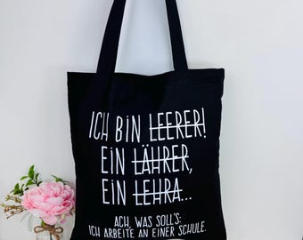 May include: Black canvas tote bag with white text that reads "ICH BIN LEERER! EIN LÄHRER, EIN LEHRA... ACH, WAS SOLL'S: ICH ARBEITE AN EINER SCHULE."