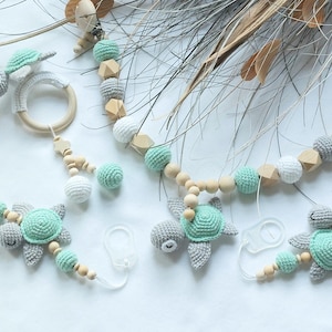 Può includere: Set di accessori per bambini con clip per ciuccio e anello per la dentizione. Gli articoli presentano tartarughe marine all'uncinetto grigie e verde menta, perline di legno e palline all'uncinetto bianche. Progettato per neonati.