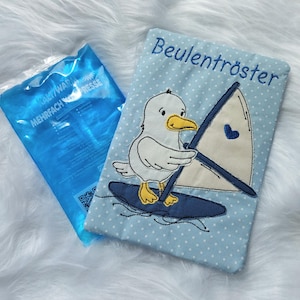 Könnte beinhalten: Ein hellblaues, gepunktetes Stoffstück mit dem gestickten Text "Beulentröster" und einer Cartoon-Möwe auf einem Surfbrett. Neben dem Stoffartikel befindet sich ein blaues Gelpack.