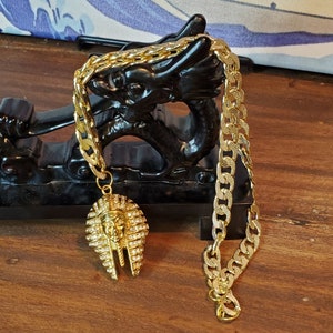 Egyptian Pharoah Mask on Flat Curb Chain. 22 inches in length, Chunky Cuban Link Style. Mask is gold 304 Stainless with Swarovski Crystals