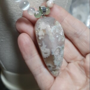 May include: A necklace with white and green beads and a large, light gray agate pendant with white and green inclusions.