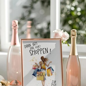 May include: A white framed picture with a rose gold border. The picture shows a woman carrying shopping bags with the text "Dann geh mal kurz shoppen!" and "F&uuml;r dich".