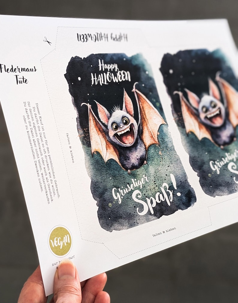 May include: Printable Halloween party favor bags featuring a cute cartoon bat with the text "Happy Halloween" and "Gruseliger Spa&szlig;!" (German for "Spooky Fun!"). The bags are designed to be folded and glued together.