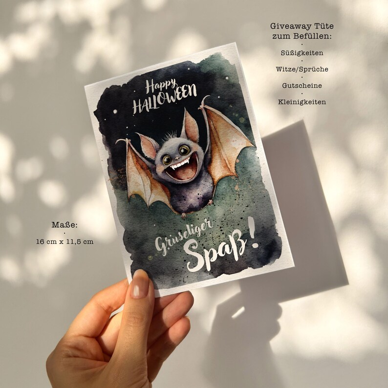 May include: A watercolor illustration of a cute, grinning bat with large, orange wings. The bat is flying against a dark green background with stars. The text "Happy Halloween" is written in black at the top of the card. The text "Gruseliger Spa&szlig;!" is written in black at the bottom of the card. The card measures 16 inches by 11.5 inches.