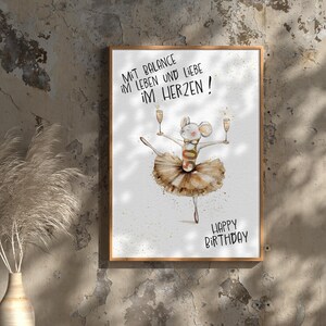 May include: A white card with a brown wooden frame. The card has a watercolor illustration of a mouse wearing a tutu and holding two glasses of champagne. The text on the card reads "Mit Balance im Leben und Liebe im Herzen! Happy Birthday!"