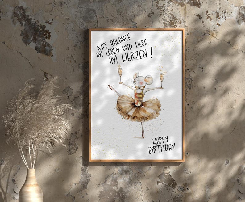 May include: A white card with a brown wooden frame. The card has a watercolor illustration of a mouse wearing a tutu and holding two glasses of champagne. The text on the card reads "Mit Balance im Leben und Liebe im Herzen! Happy Birthday!"
